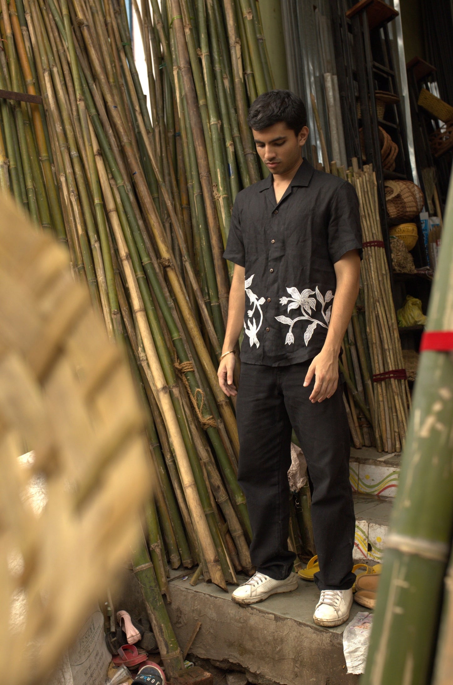 Soham in an embroidered black linen shirt standing in a bamboo shop