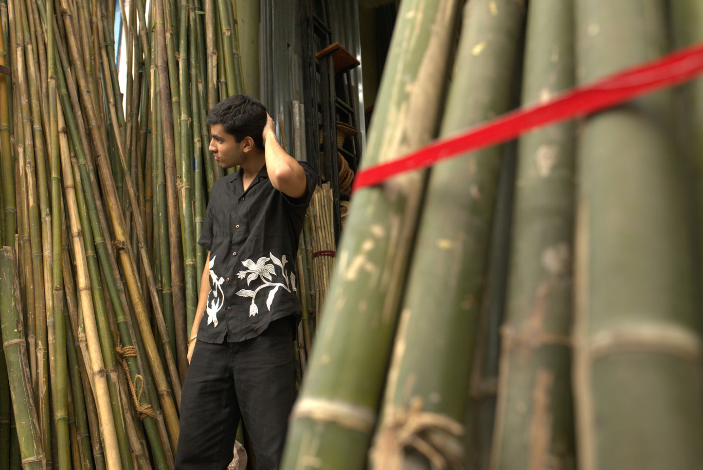 Side details of Soham in a black linen shirt standing in a bamboo shop