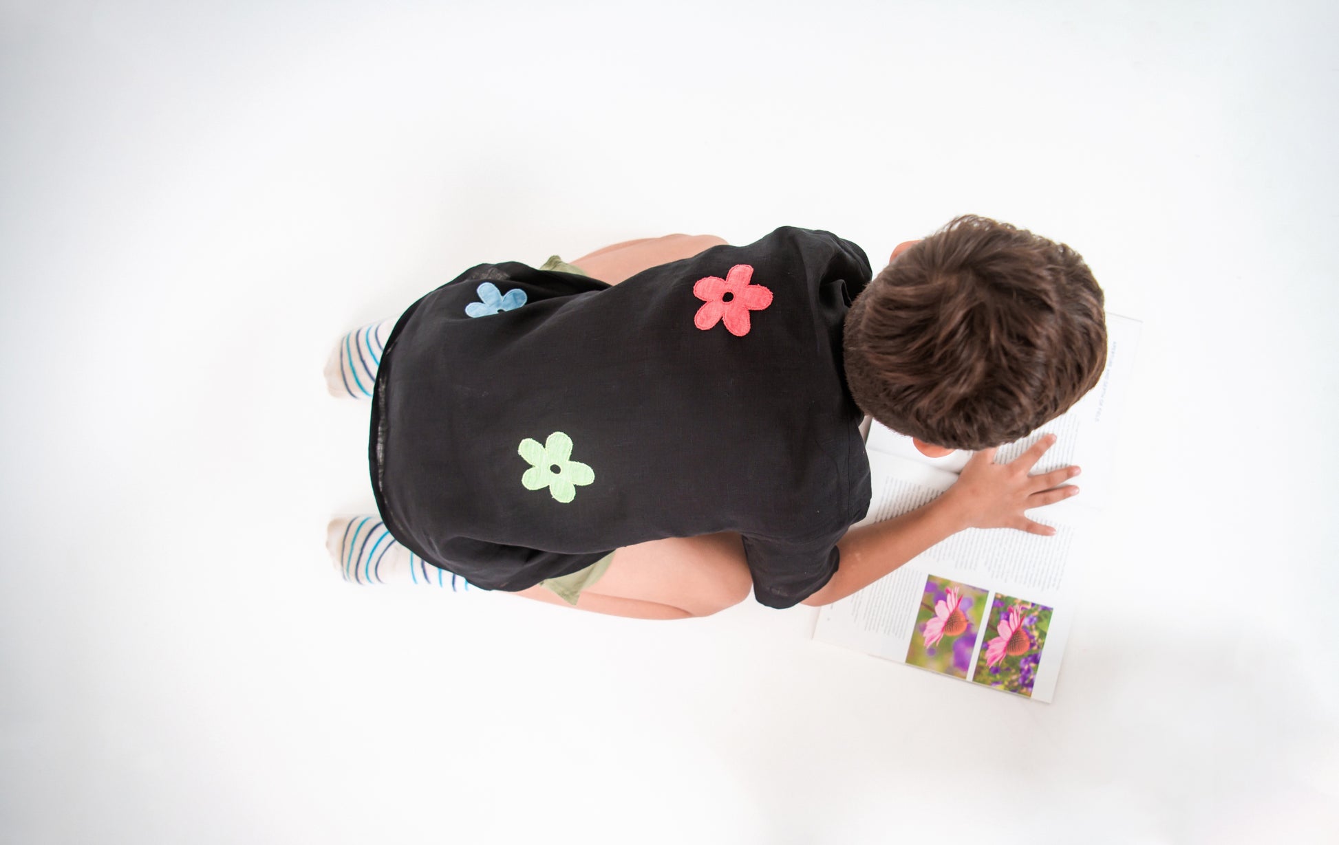 details of the back of a young 5-6 year old boy in a floral black linen shirt sitting and reading