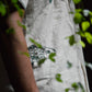 details of a half-sleeved beige linen shirt with a detailed green fish embroidered across the centre of the shirt  and a smaller fish peeking from the left bottom corner