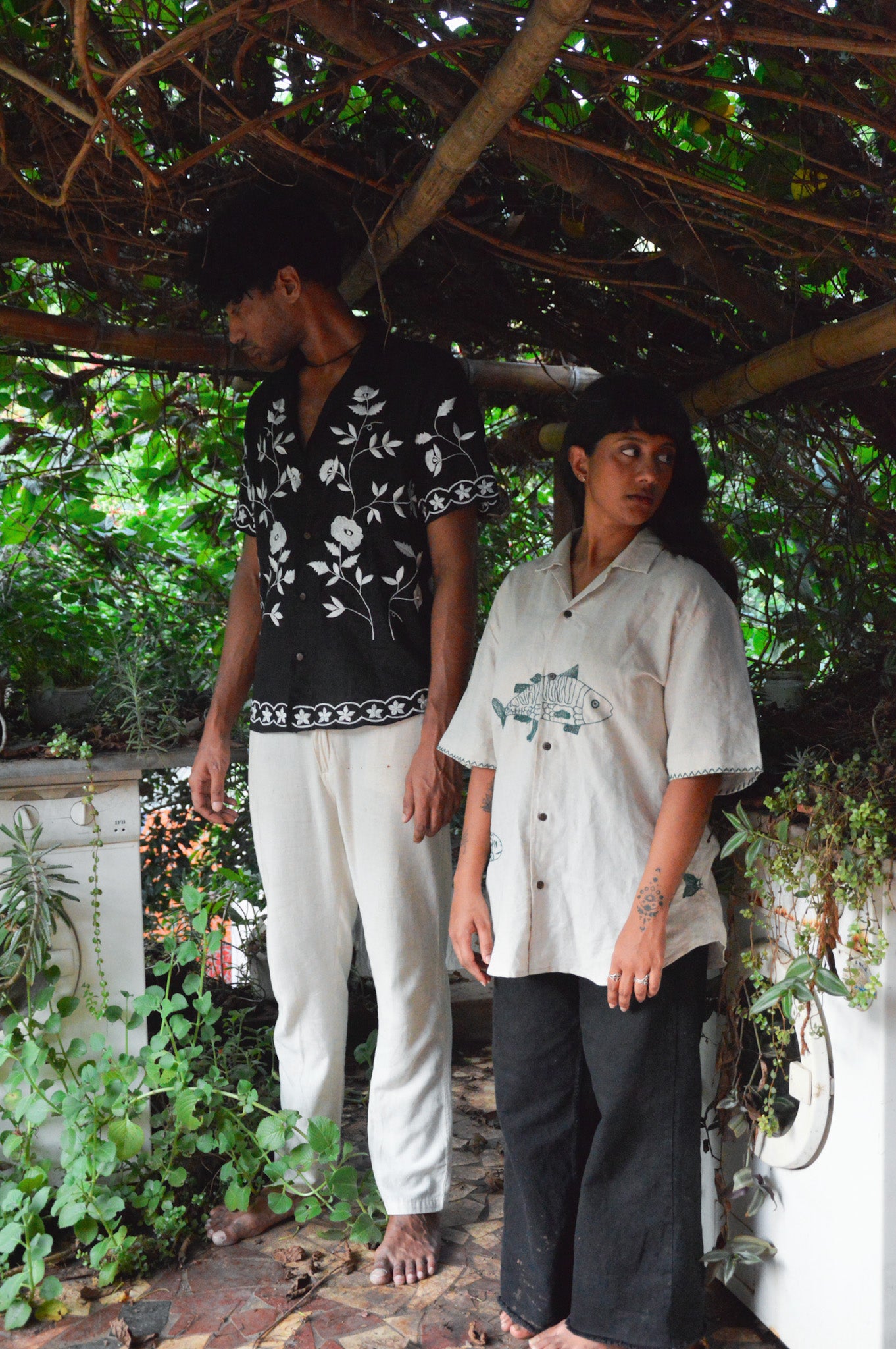 A boy and a girl in black and beige embroidered linen shirts are standing in an outdoor kitchen garden