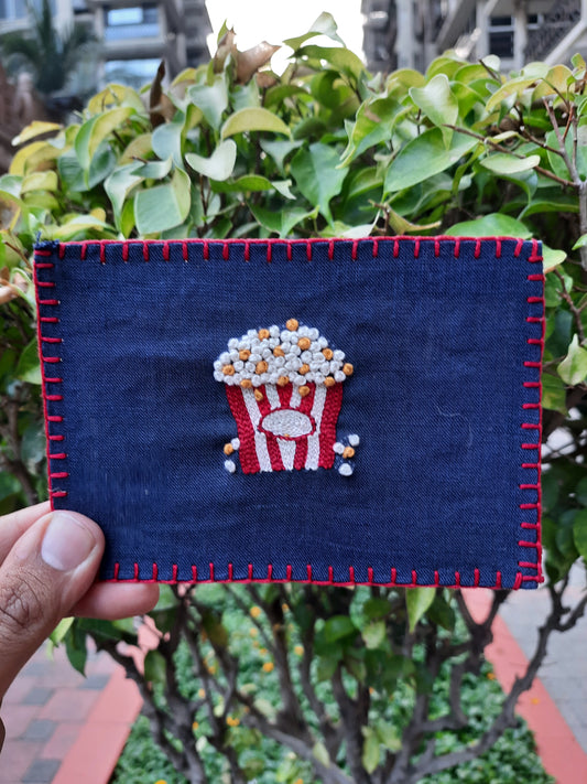 Hand-embroidered postcard featuring a colorful popcorn bucket, crafted from sustainable linen, perfect for movie lovers