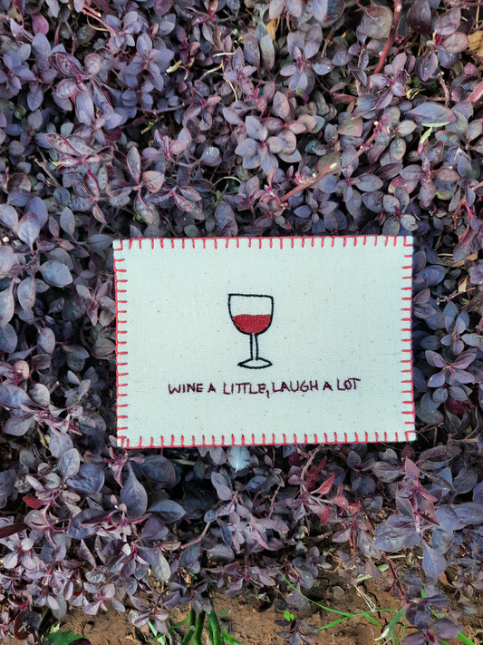 Hand-embroidered postcard featuring a wine glass with the phrase 'Wine a Little, Laugh a Lot,' crafted from sustainable linen, ideal for sending festive and cheerful messages