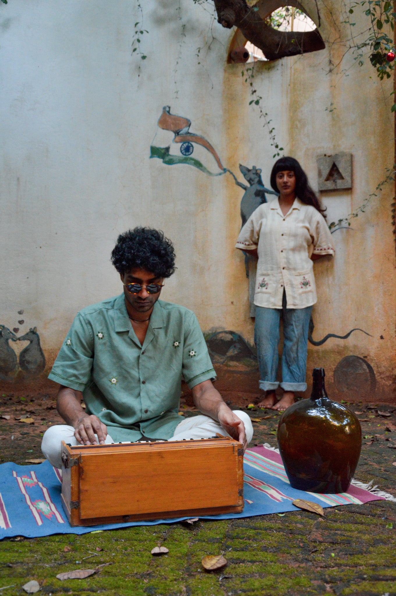 A young man in green linen shirt with flowers embroidered throughout is playing the harmonium