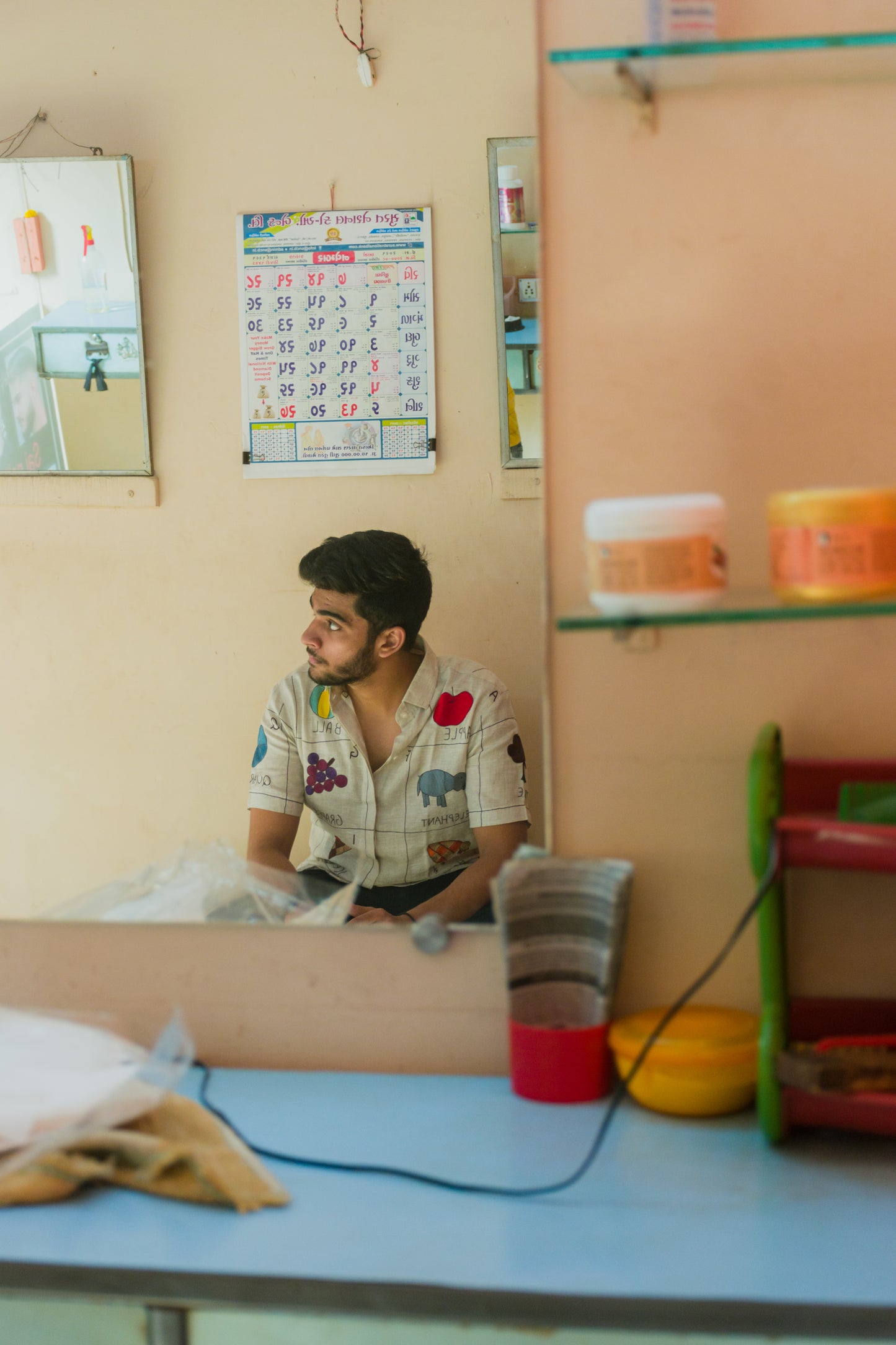 A young man in an beige linen shirt with the hand-embroidered alphabet is sitting in a shop