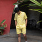 a front view of a man wearing co-ordinated pair of yellow linen shirt and shorts with green sun embroidery at a cafe