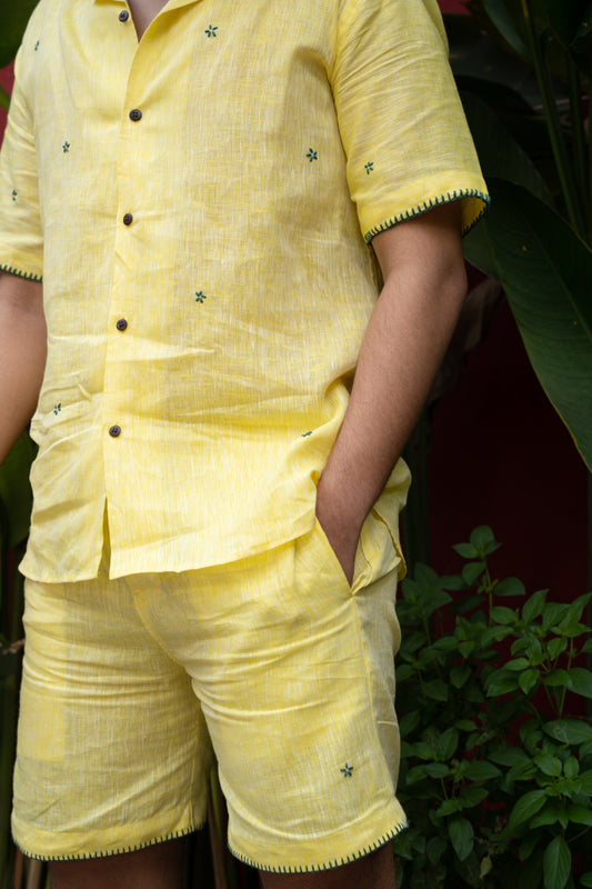 a detailed shot of a man wearing co-ordinated pair of yellow linen shirt and shorts with green sun embroidery. Front view