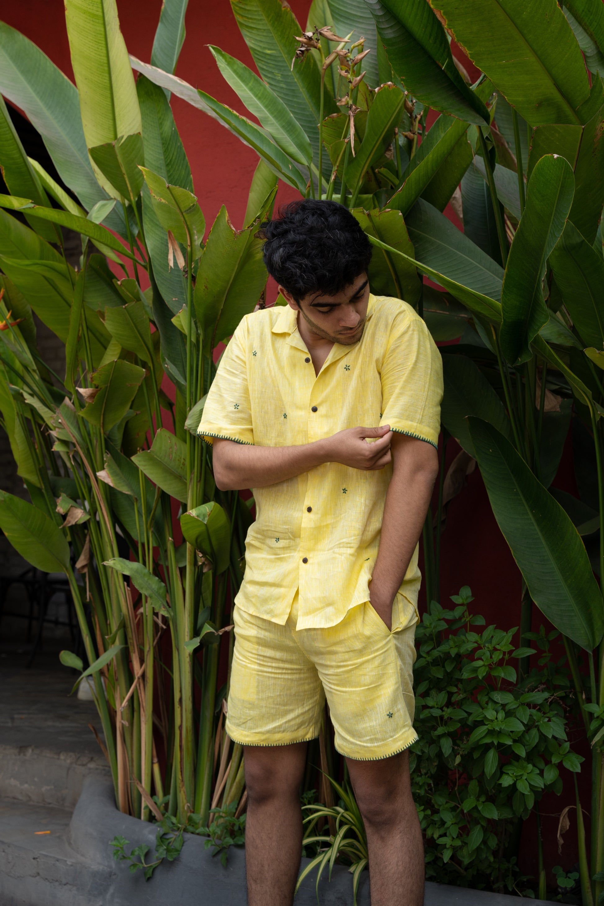 a Front view of a man wearing co-ordinated pair of yellow linen shirt and shorts with green sun embroidery and green border on the sleeves.