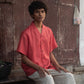 closer shot of a man in a rich red linen half-sleeved shirt is sitting in front of a wide brown door