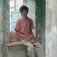 A man in peach linen half-sleeved cuban collared shirt sitting in a green arch