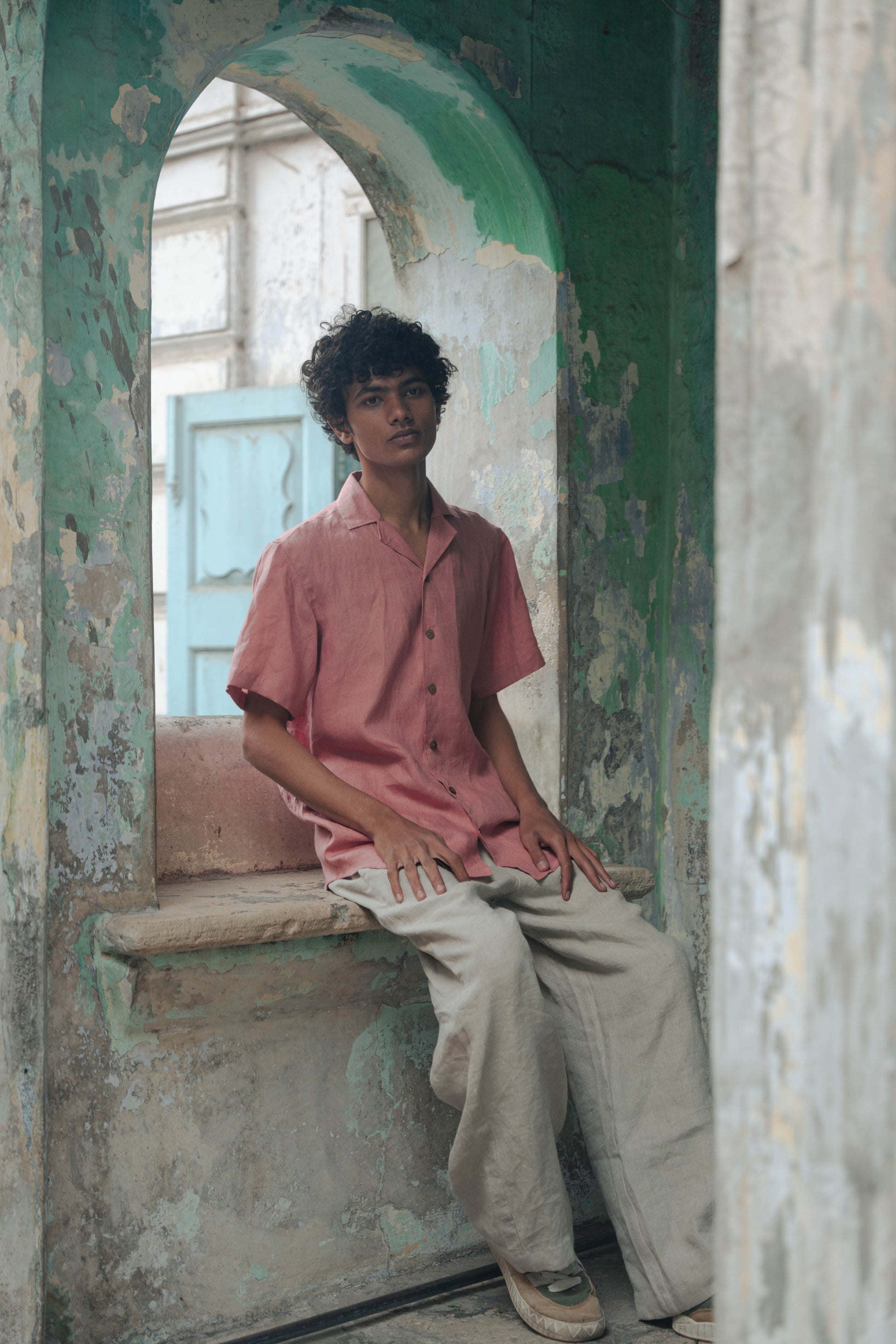 A man in peach linen half-sleeved cuban collared shirt sitting in a green arch