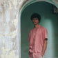 Closer look of a man in peach linen half-sleeved cuban collared shirt standing in an arch with green background