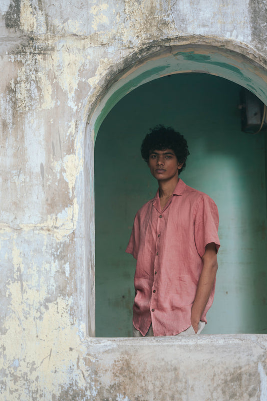 Closer look of a man in peach linen half-sleeved cuban collared shirt standing in an arch with green background