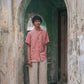 A man in peach linen half-sleeved cuban collared shirt standing in front of a door to a rustic house