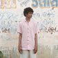 A man in light pink half-sleeved cuban collared linen shirt and white linen pants in front of a graffiti wall