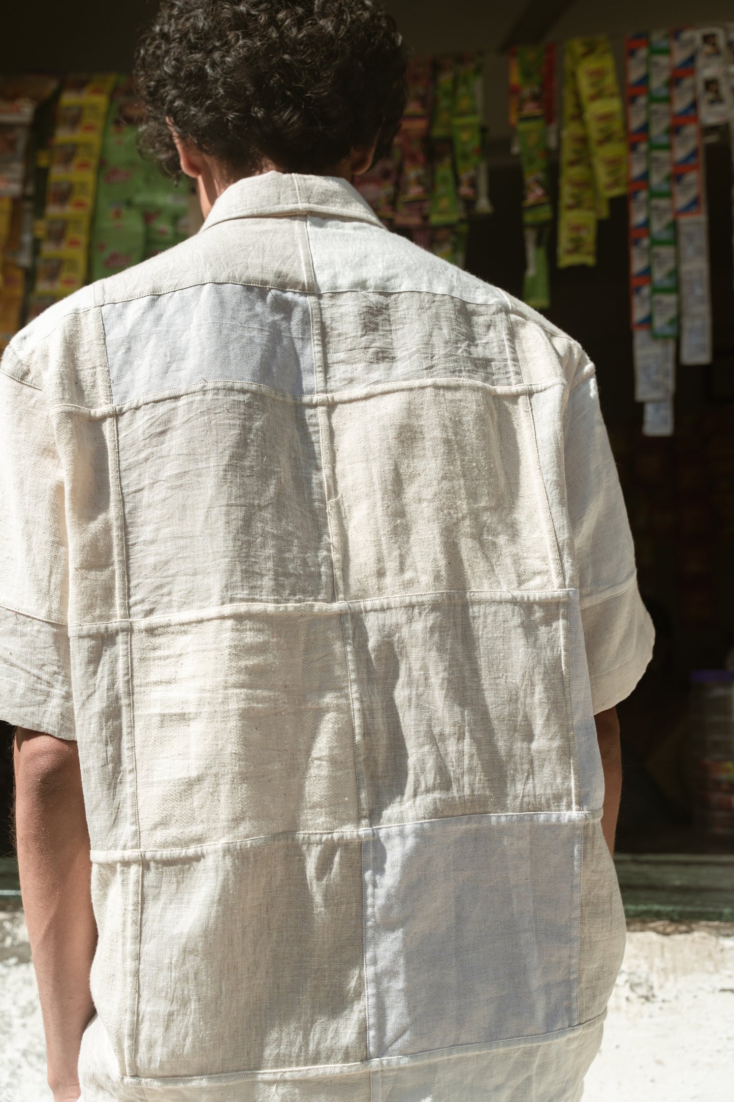 Back of a young man in an off-white half-sleeved shirt made with patches of cotton and linen squares