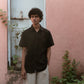 Closer look of a man in a black linen half-sleeve regular collar shirt is standing infront a pink wall with a blue door