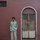 Wider shot of A man in mint-green pure linen full-sleeved shirt and light beige linen pants is standing in front of a pink wall