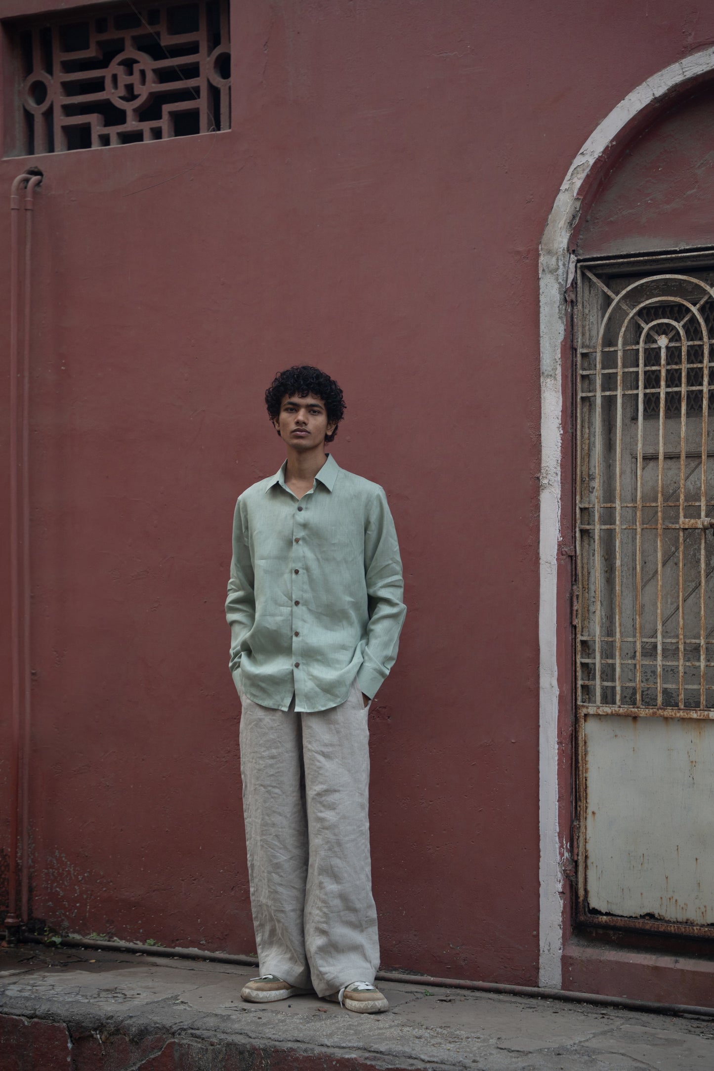 A man in mint-green pure linen full-sleeved shirt is standing in front of a pink wall