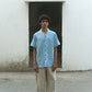 A man in blue linen cuban collared half sleeve shirt is standing in front of a off white wall