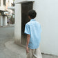 Back shot of a man in a blue linen shirts and off-white pants walking on the streets