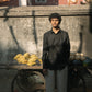 A man in a black linen full-sleeve regular collar shirt is standing in front of a cart with bananas and melons