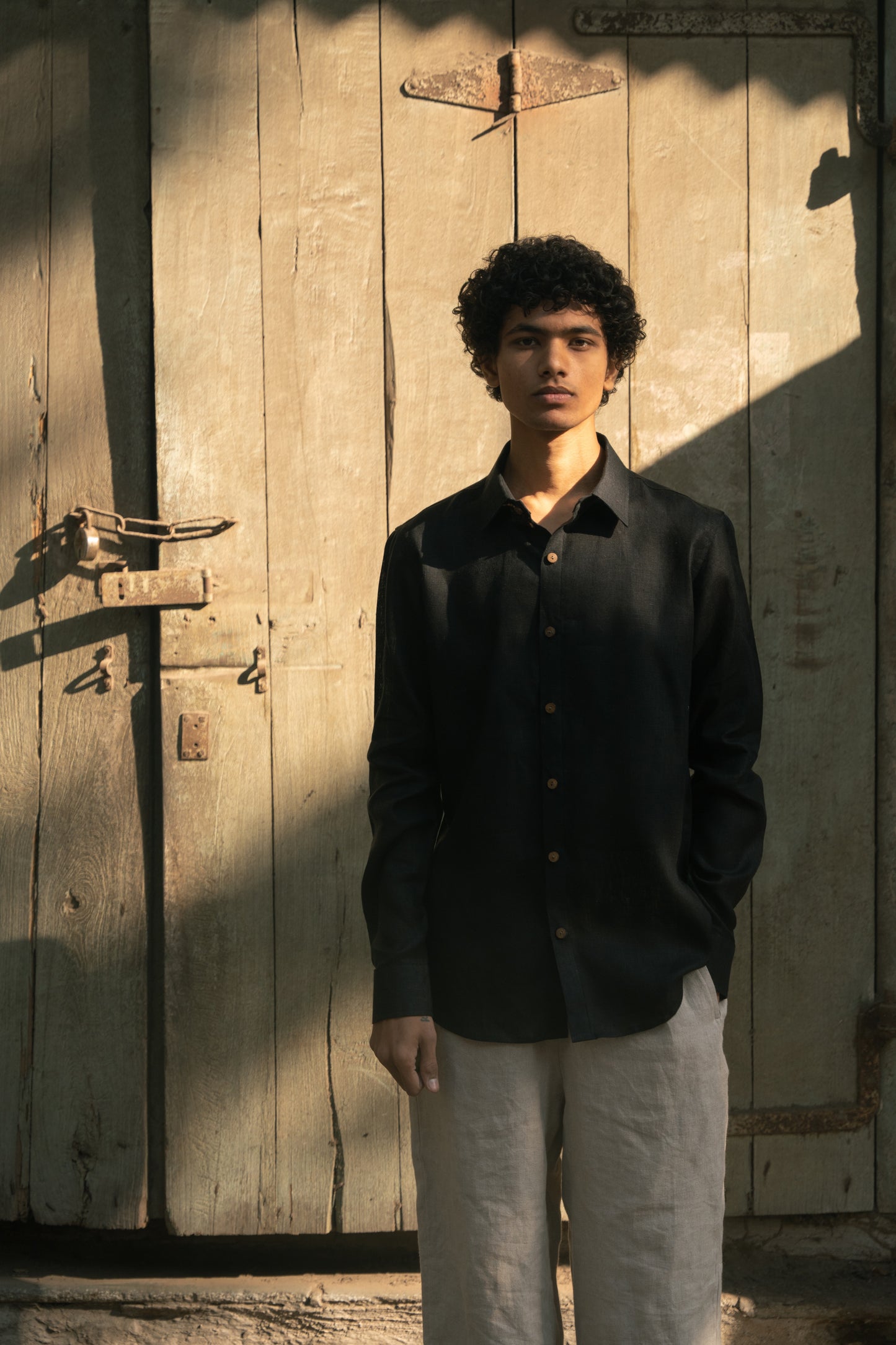 closer look of a man in a black linen full-sleeve regular collar shirt is standing in front of a mint green door