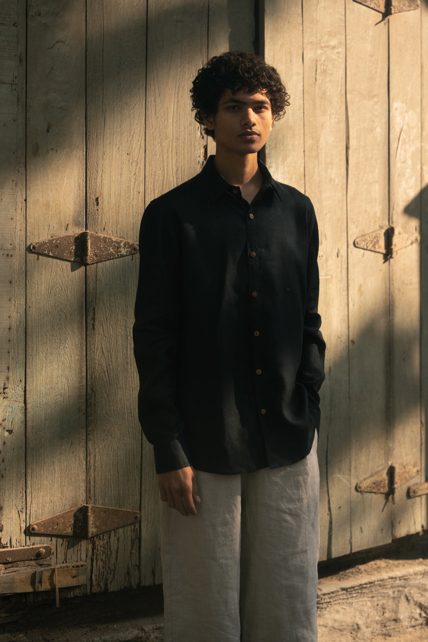 A man in a black linen full-sleeve regular collar shirt is standing in front of a mint green door