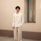 A wider shot of a man in light beige full sleeved pure linen shirt and a darker beige pants standing in front  of a wall