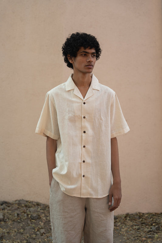 A man in white hand-woven cotton shirt with a cuban collar standing in front of a peach wall