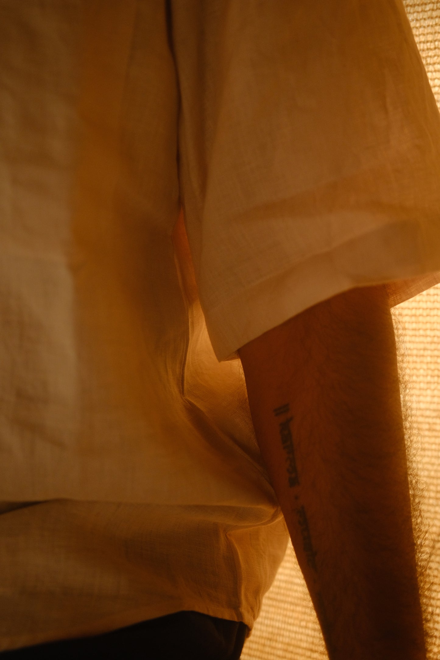 Close up of the half sleeve detail of an off-white linen shirt worn by a man in a soft light