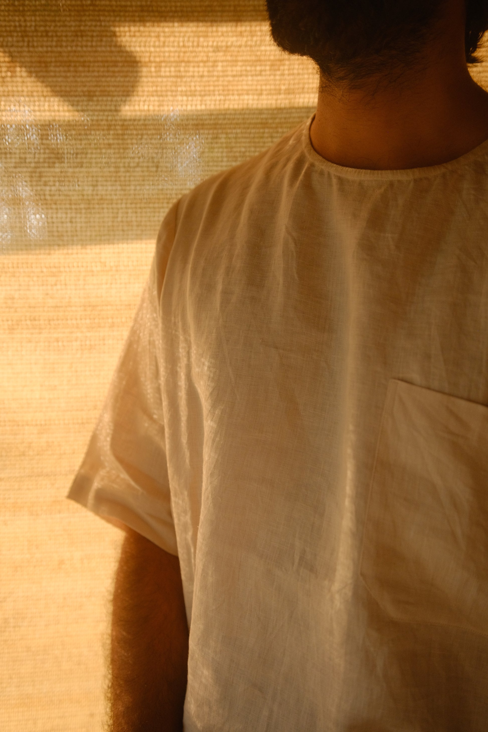 A man in offwhite pure linen t-shirt featuring a left pocket standing in soft light