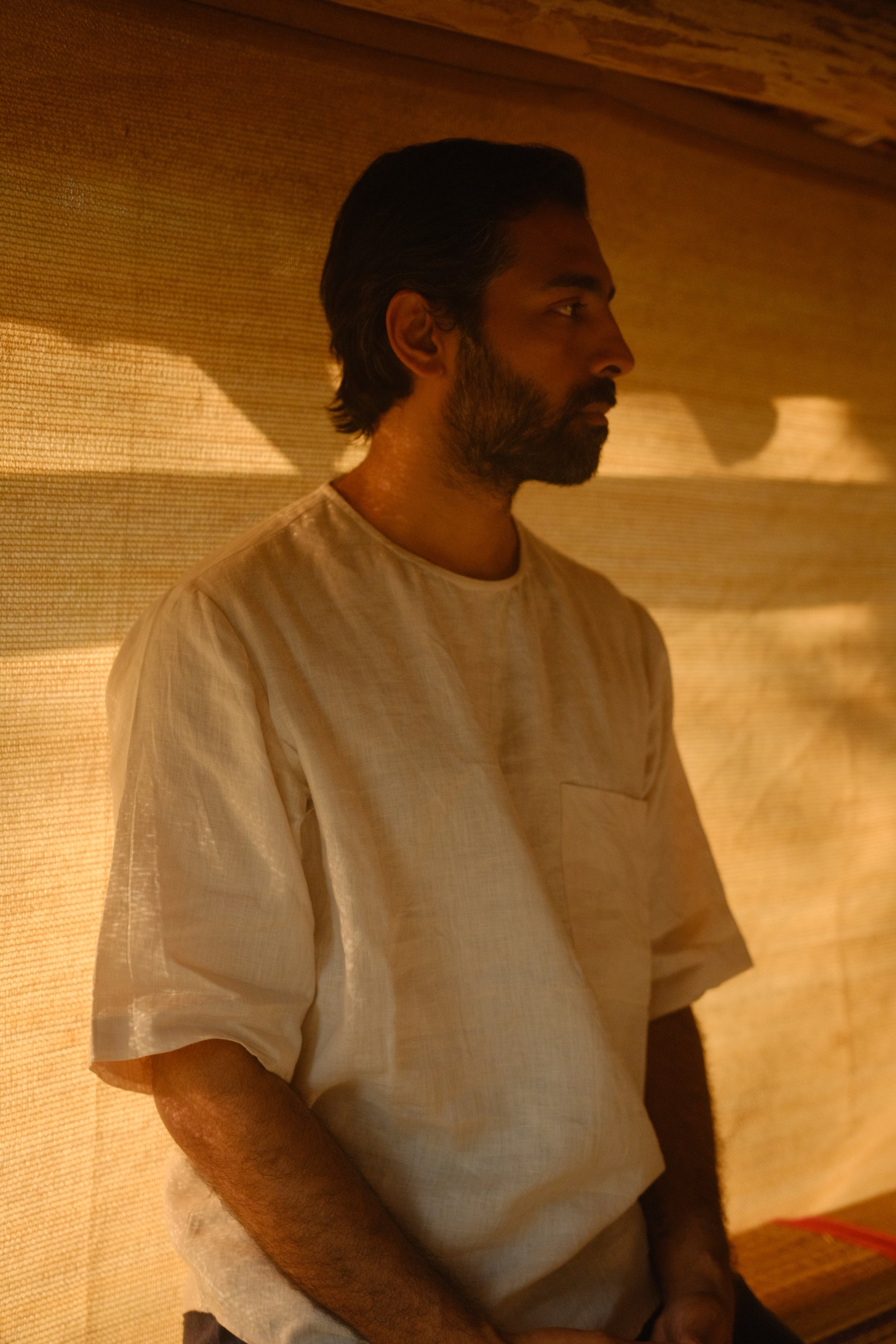 a man in off-white linen t-shirt sitting on a wooden bench