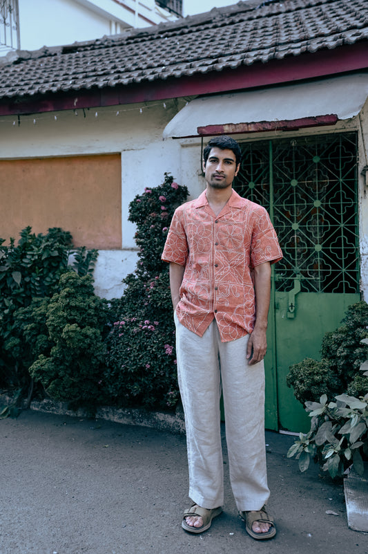 A young man in a burnt orange hand-embroidered linen shirt standing in front of a beautiful rustic house