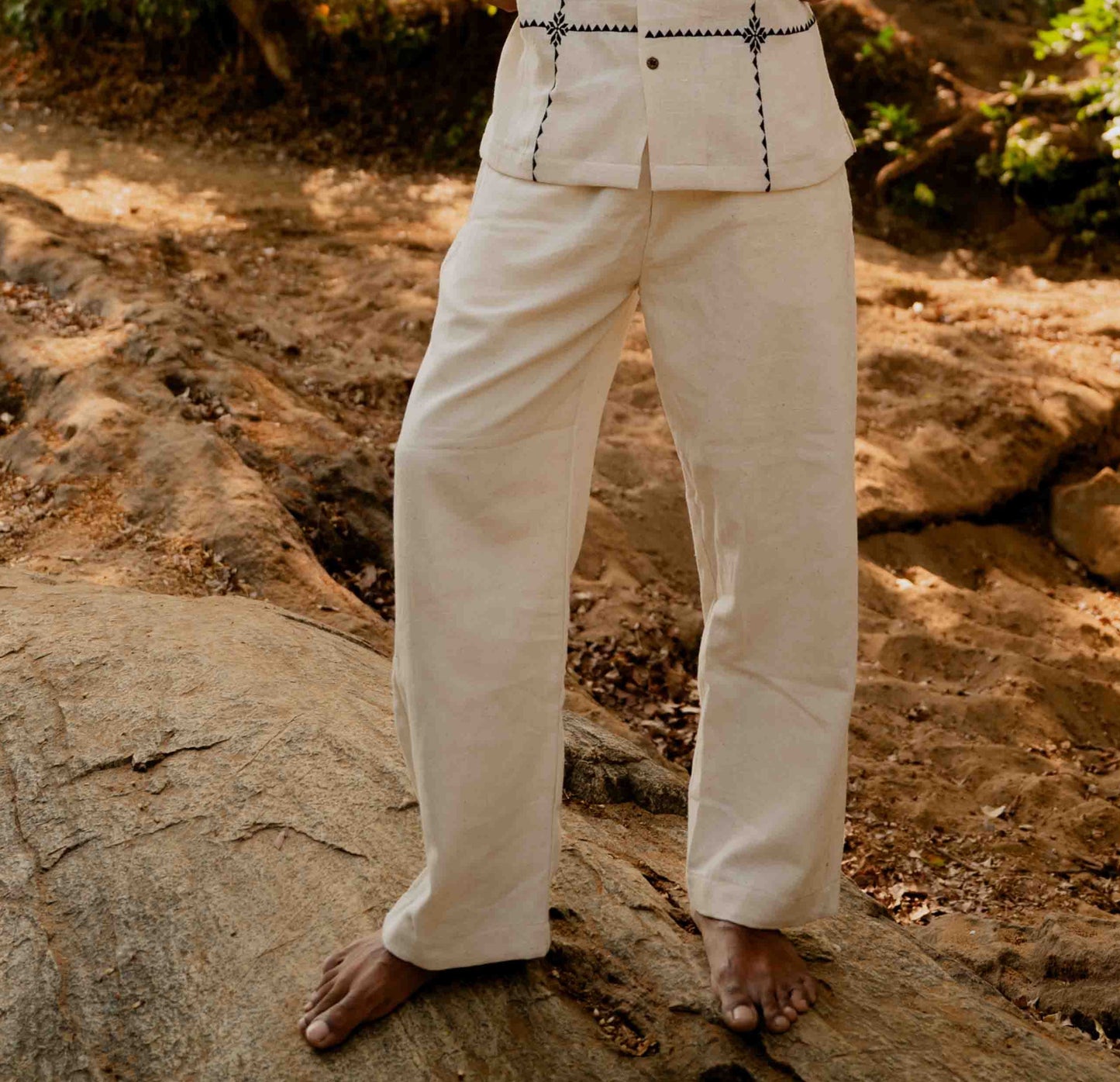 A man standing on a rock wearing off-white kala cotton hand-woven pants. Front view