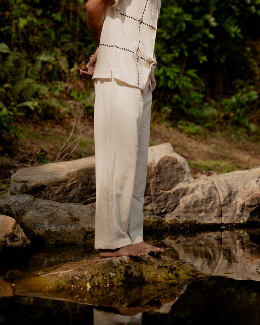 Side view of a man standing near a riverfront wearing off-white hand-woven kala cotton pants.