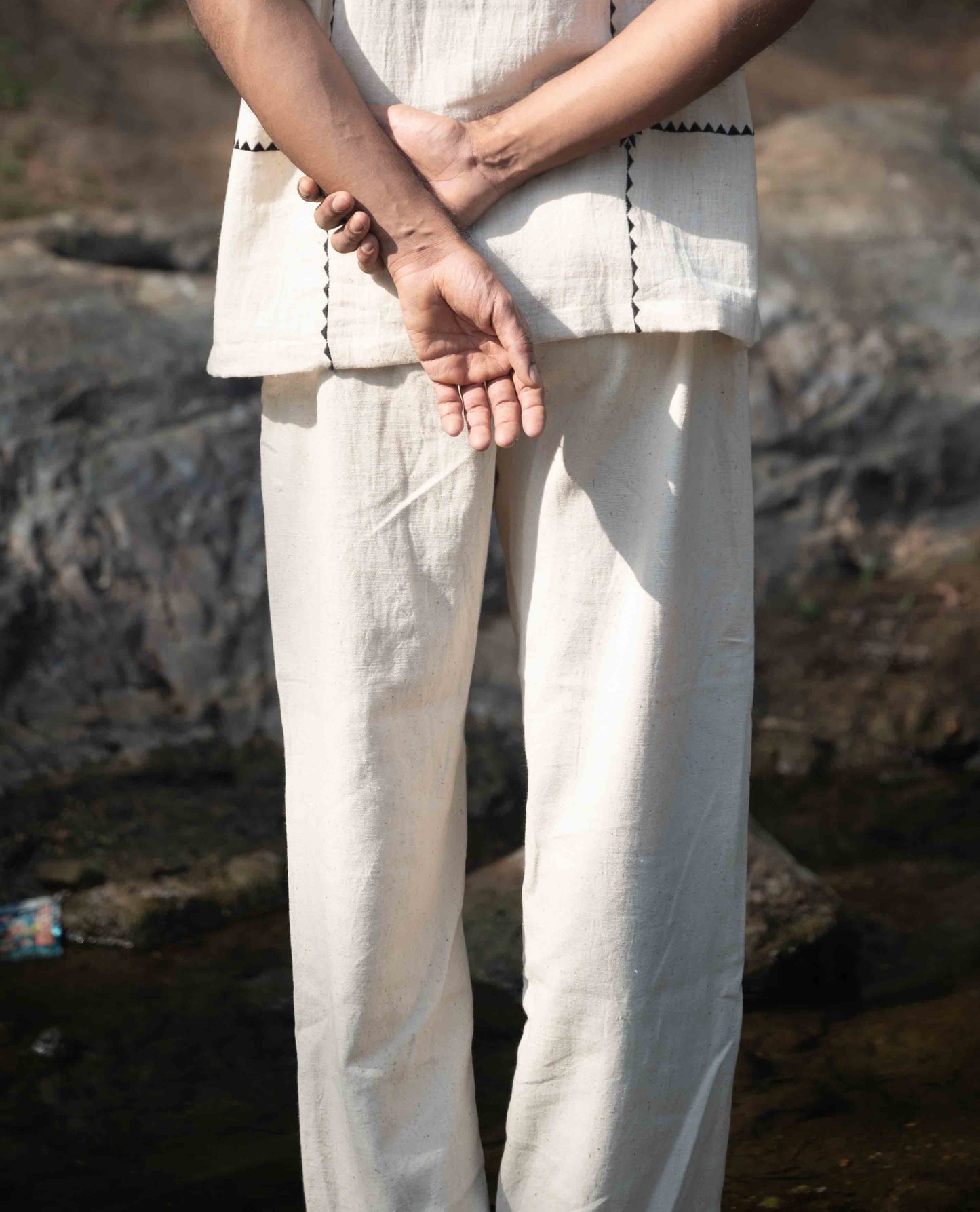 Back view of a man standing on a rock wearing off-white hand-woven kala cotton pants.