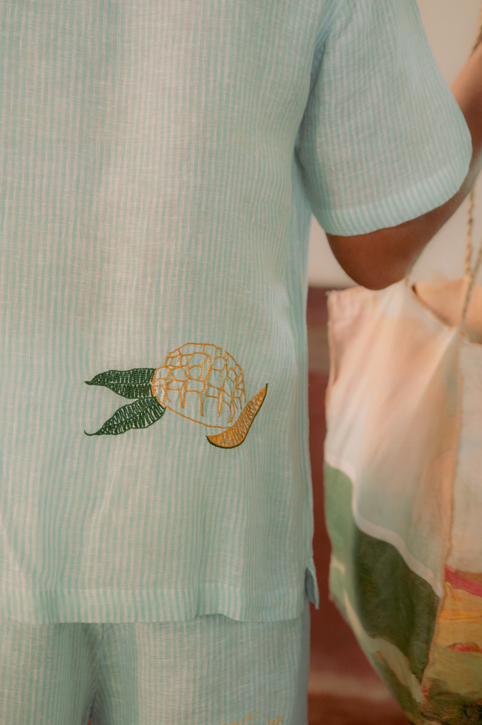 Detailed back view of green and white stripes linen shirt with embroidered mango.