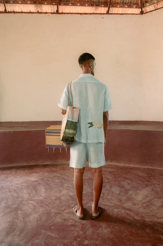 Detailed back view of a man in a yoga hall wearing green and white stripes linen co-ordinated set of shirt and shorts with embroidered mango.