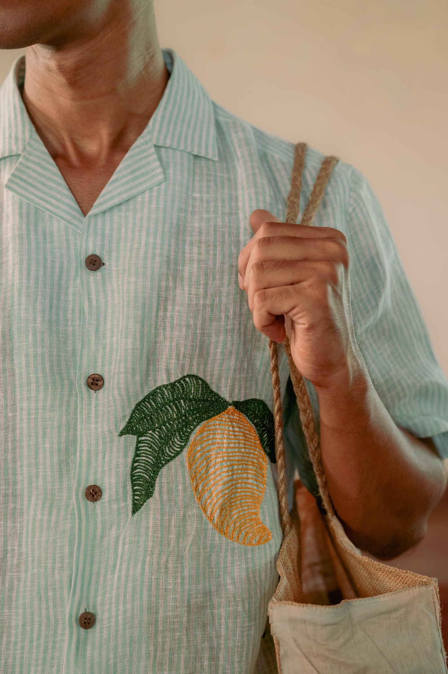 a man wearing  green and white stripe linen shirt with embroidered mangoes. Detailed view