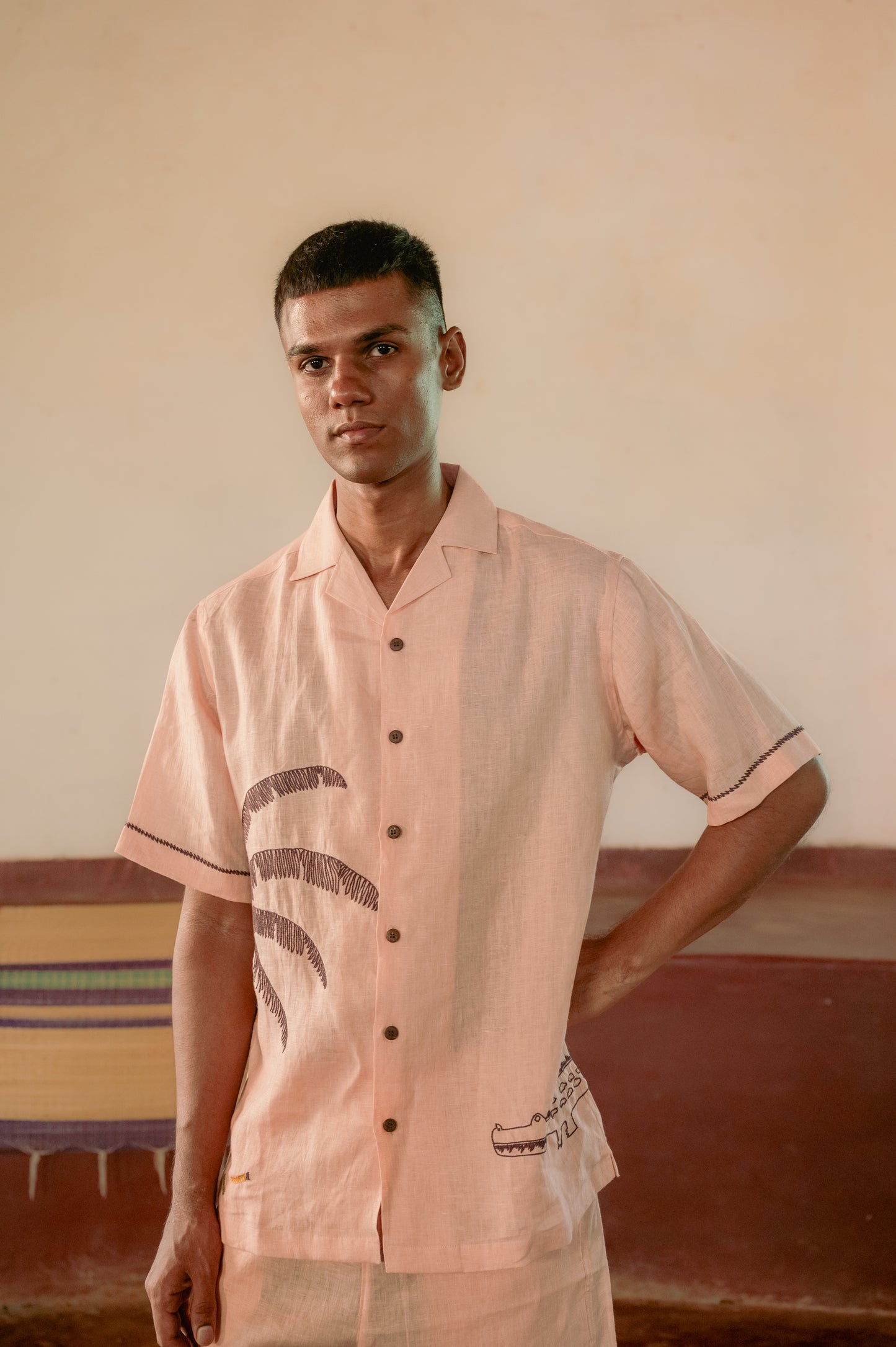 A man in a peach linen shirt which has a crocodile and a banana tree embroidered on each of its fronts