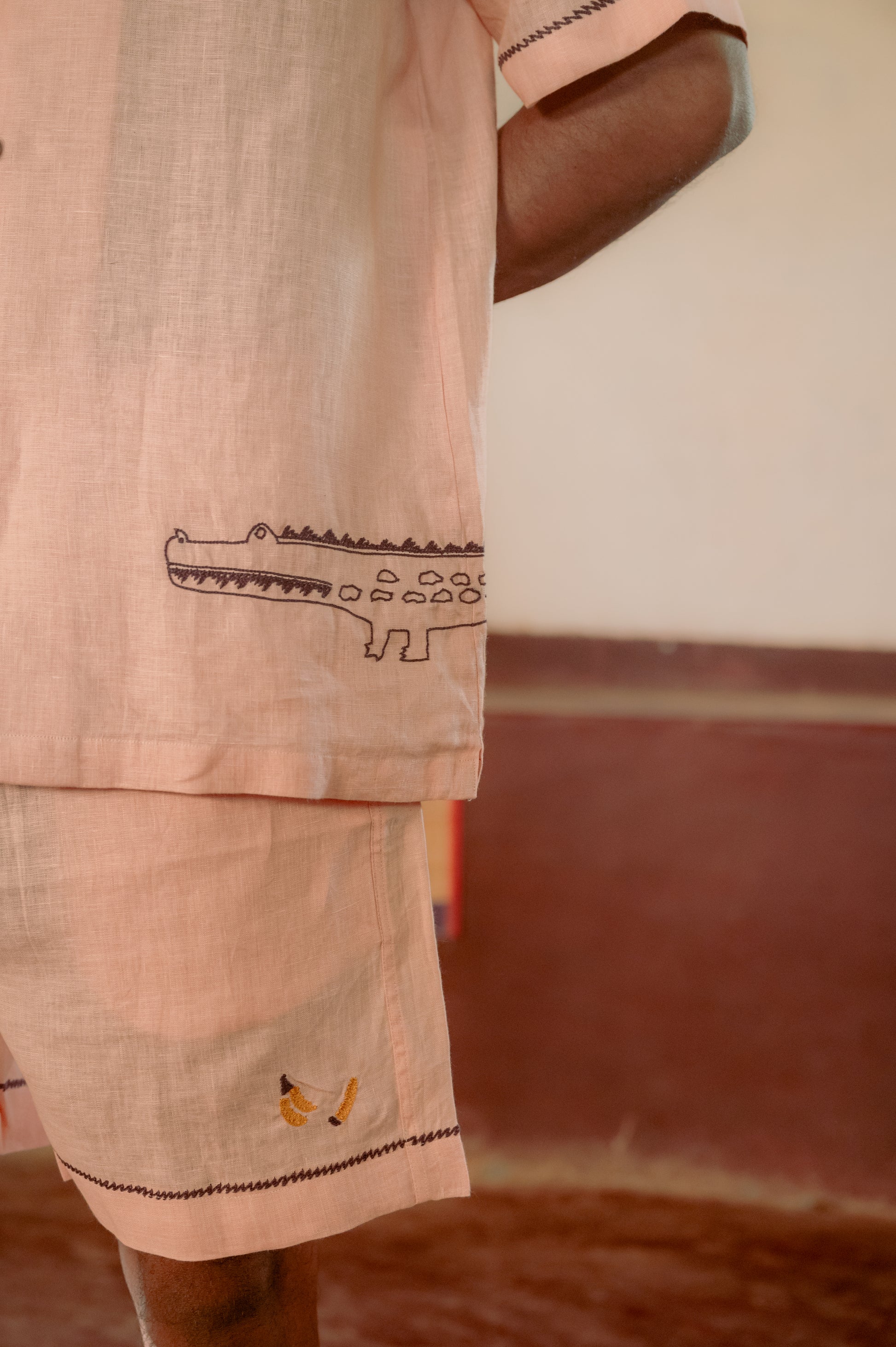 Detailed side view of the left front of a peach linen shirt with an embroidery of a purple crocodile