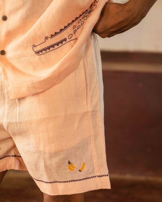 Detailed front view of peach linen shorts with hand-embroidered bananas.