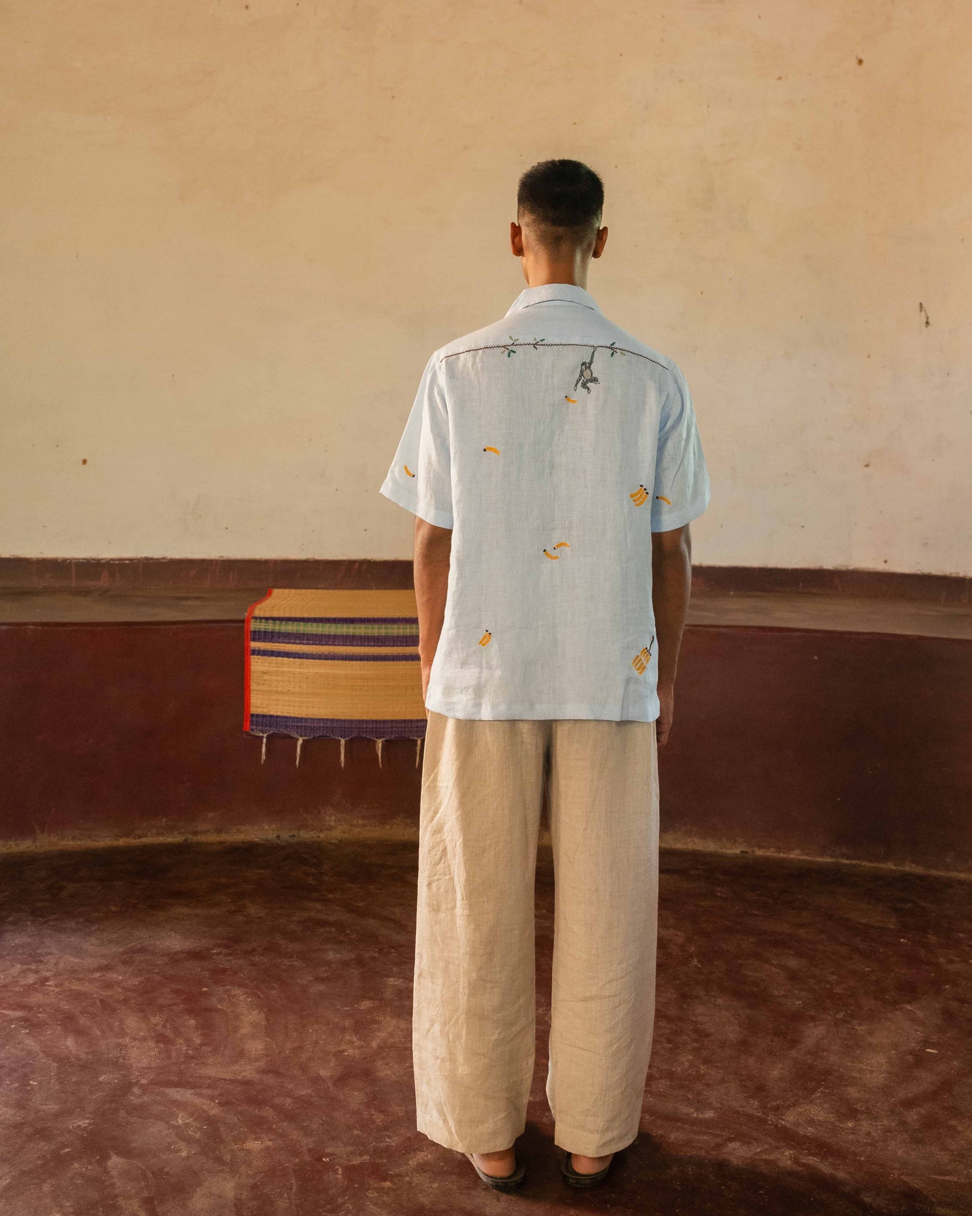 A man in eco-friendly, monkey business hand-embroidered linen shirt in a yoga hall. half sleeves shirt, Material: linen, back view