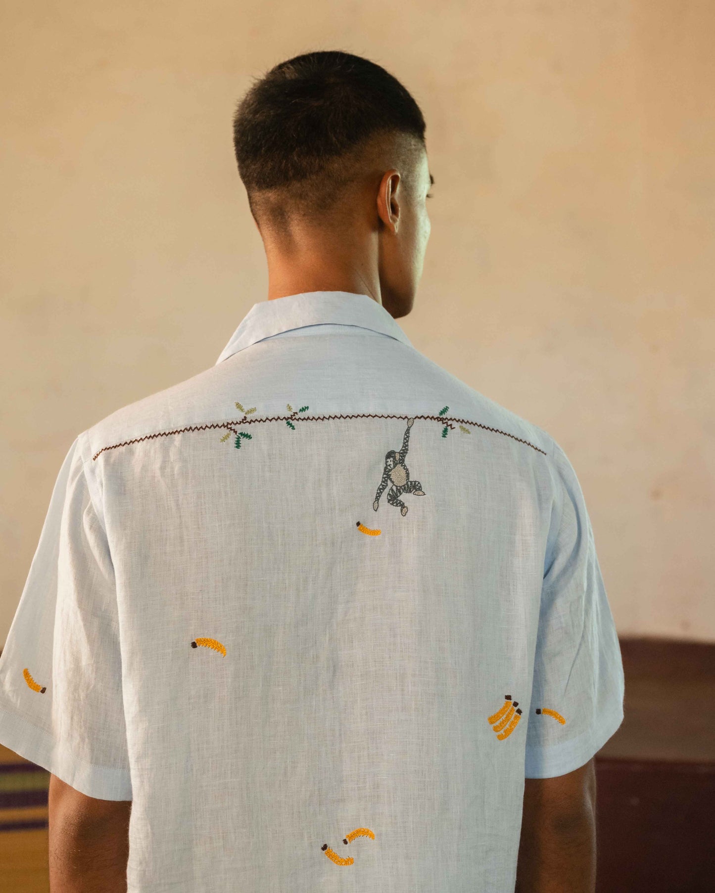 A man in eco-friendly, monkey business hand-embroidered linen shirt in a yoga hall. half sleeves shirt, Material: linen, back view