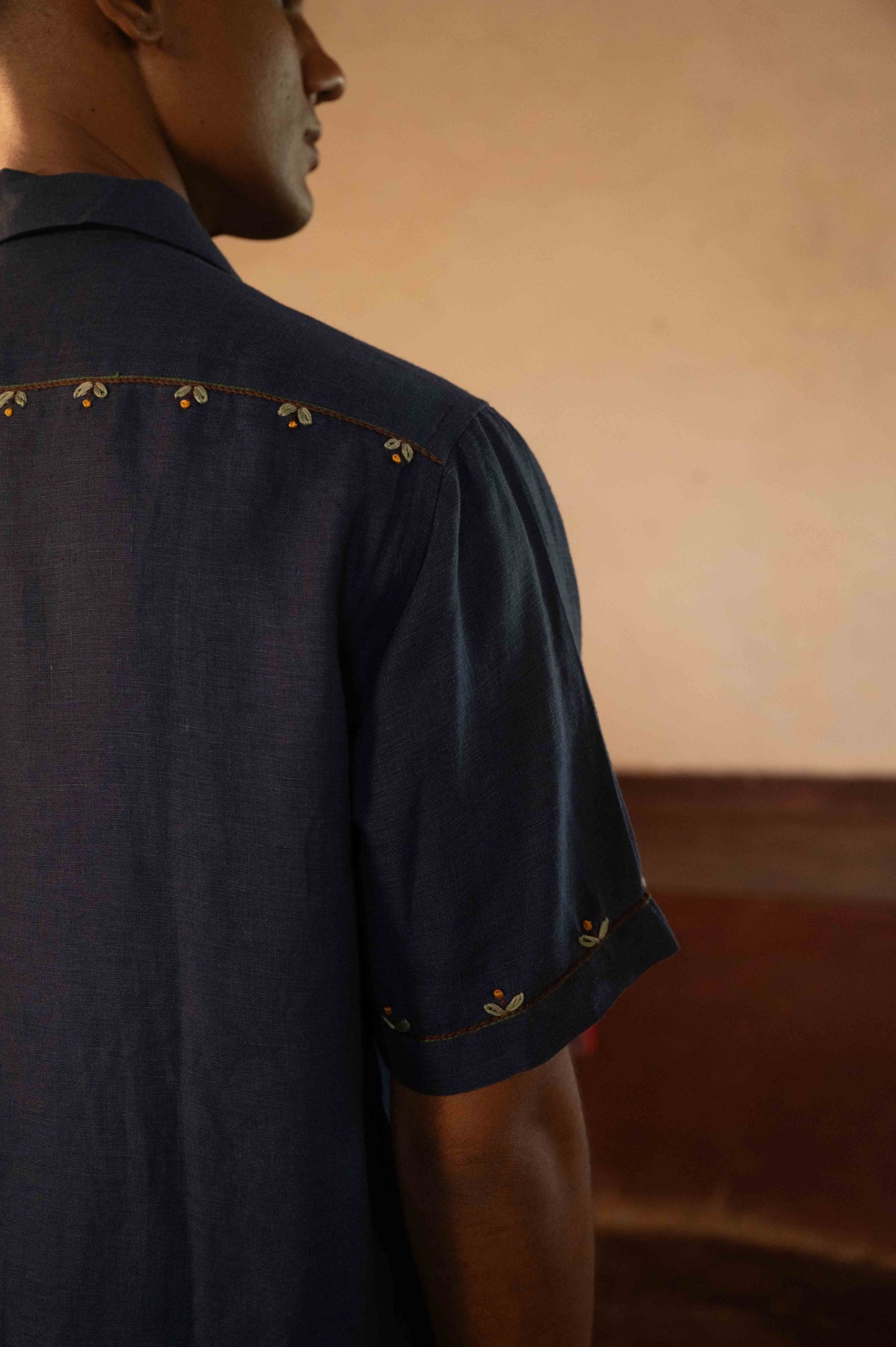 A man in eco-friendly, buds in blue hand-embroidered linen shirt in a yoga hall. half sleeves shirt, Material: linen, back detailed view