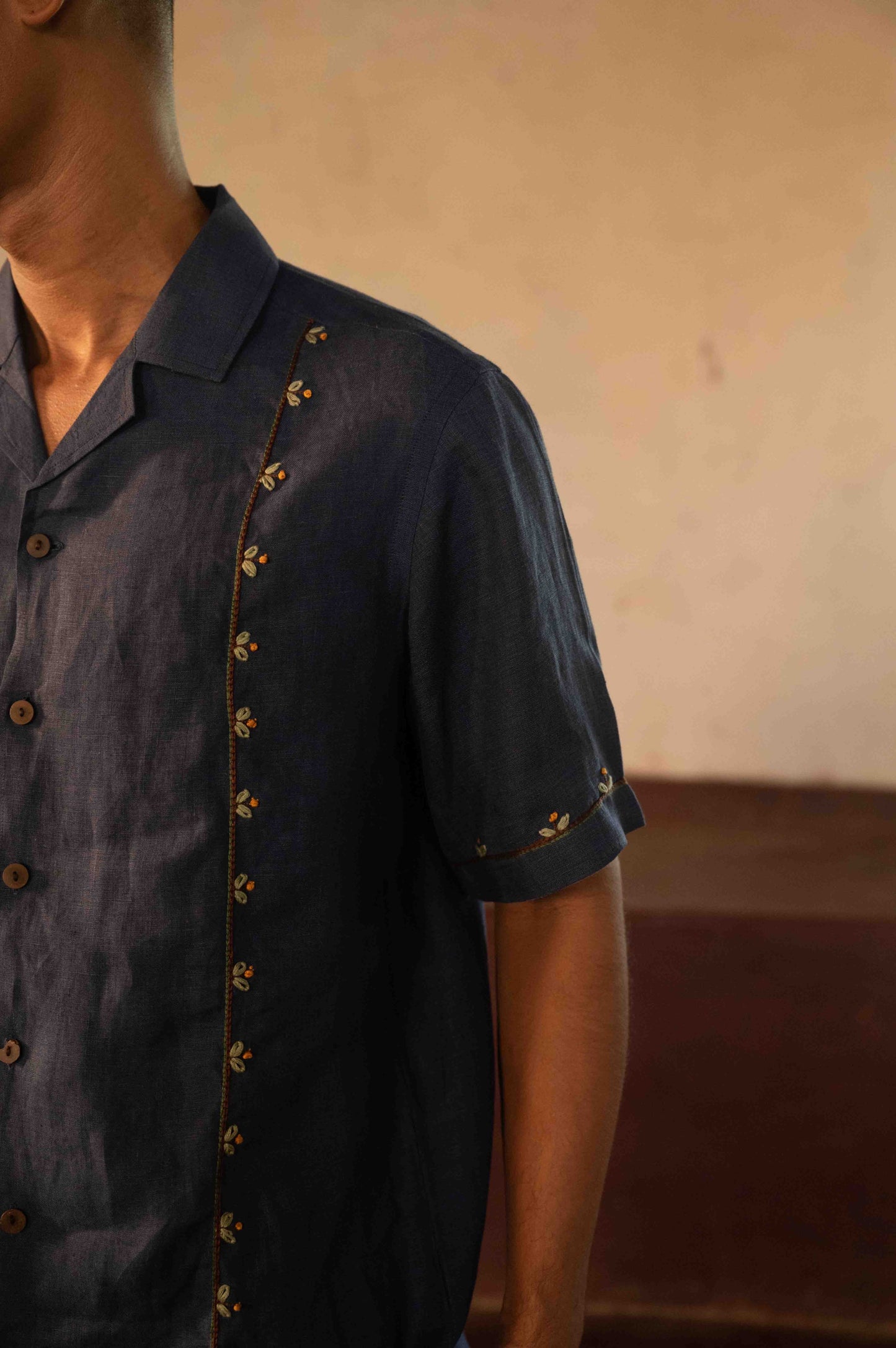 A man in eco-friendly, buds in blue hand-embroidered linen shirt in a yoga hall. half sleeves shirt, Material: linen, front detailed view