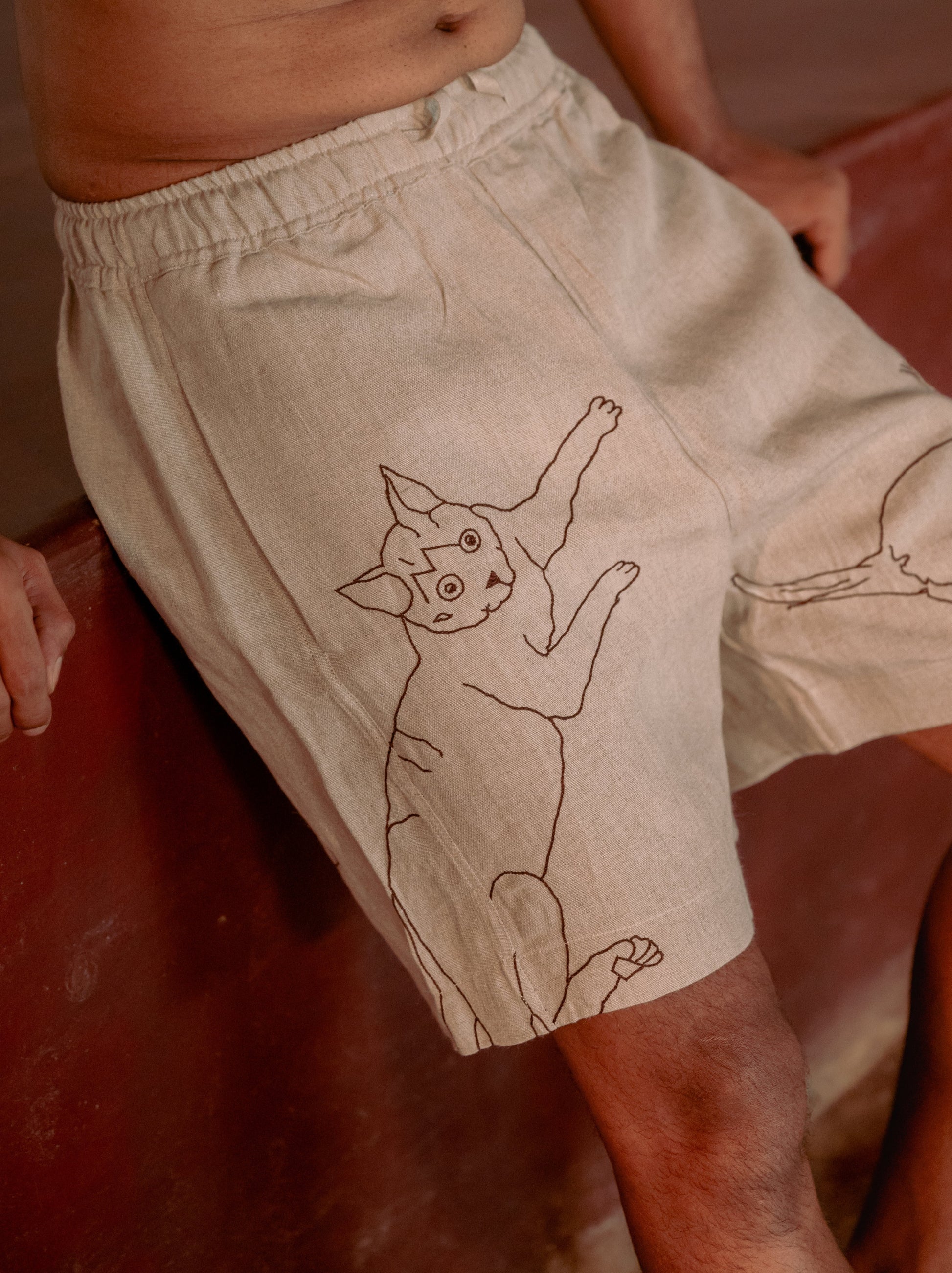 a detailed image of a a man in beige linen shorts with embroidered cats. Front view