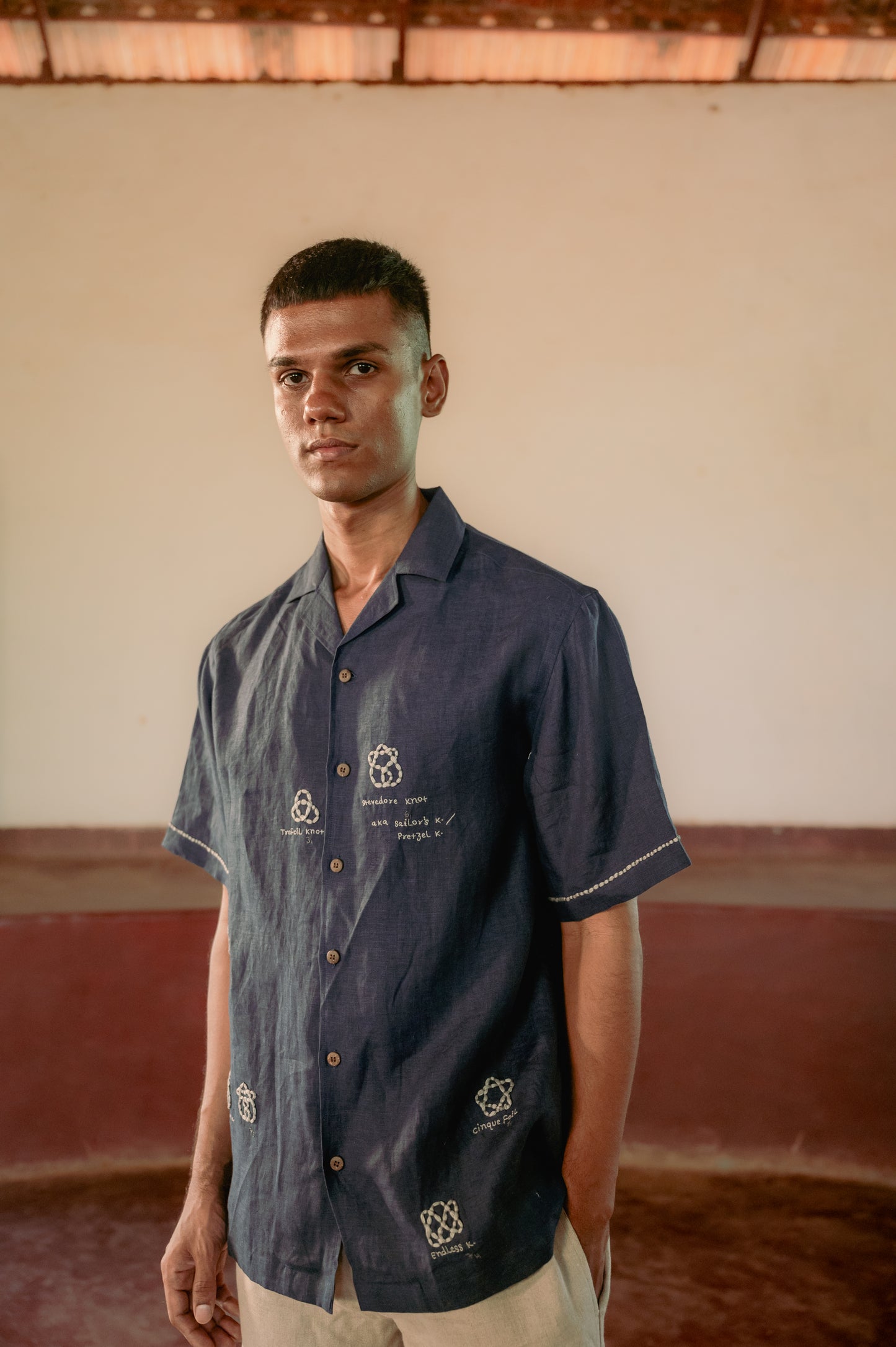 Side look of a man in a blue linen shirt with an embroidery inspired by the Knot theory 