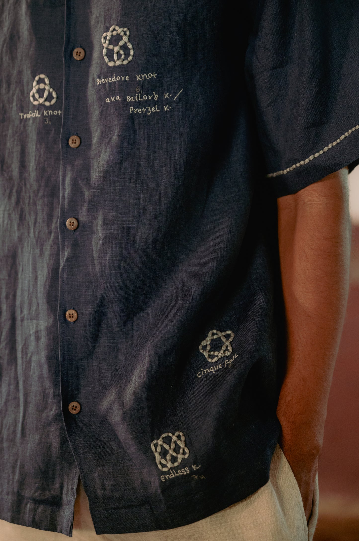 Detail zoomed in view of the embroidery inspired by the Knot theory on a blue linen shirt 